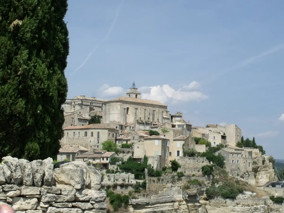 Stone castle facade in Gordes with a tower and trees under a blue sky