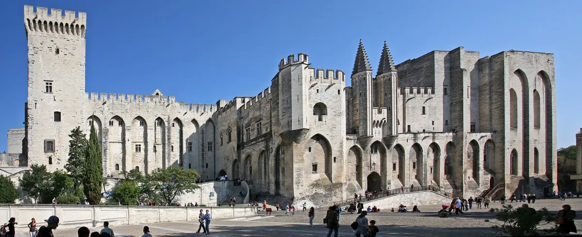 Gothic stone facade of the Palais des Papes beside a wide sunny square