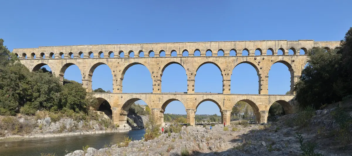Pont du Gard aqueduct over a calm river with wooded hills on both sides