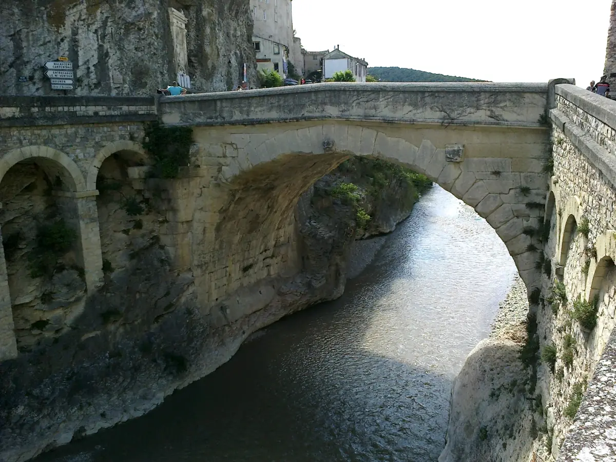 Single-arch Roman bridge crossing a narrow river gorge below rock walls
